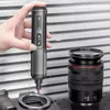 A hand is holding a cordless screwdriver, which is being used to tighten a screw on a camera lens mount. A camera lens is also visible in the background. Voir les images du produit