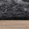 A close-up view of a dark gray shaggy rug on a wooden floor. Produktbild-Vorschau