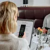 A woman is using a smartphone to scan a menu at a restaurant. Podgląd zdjęcia produktu