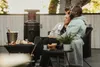 A couple sits on a patio next to a patio heater, with drinks and snacks on a table. Produktbild-Vorschau