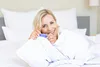 A woman is lying in bed, holding a pregnancy test. Produktbild-Vorschau