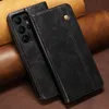 A black leather flip wallet case for a smartphone is shown in close-up, resting on a textured brown surface. Produktbild-Vorschau