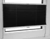 A black pleated blind is installed in a white window frame. Podgląd zdjęcia produktu
