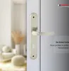 A close-up of a silver door handle with a keyhole on a door, with a blurred interior scene in the background. Produktbild-Vorschau