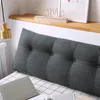 A close-up view of a gray tufted wedge pillow placed on a bed with a checkered pattern. A wooden shelf with a decorative 'home' sign and a framed picture is visible above the pillow. Produktbild-Vorschau