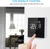 A hand is touching a digital thermostat mounted on a wall, with a room interior visible in the background. Podgląd zdjęcia produktu