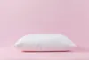 A white pillow is centered on a pink surface against a pink background. Produktbild-Vorschau
