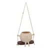 A beige, round planter with a smiling face, arms, and legs, hanging from a rope swing with a brown seat. Anteprima dell’immagine prodotto