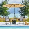 Two chairs and a table under an umbrella by a pool with a body of water and buildings in the background. Produktbild-Vorschau
