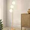 A modern floor lamp with three glass globes stands in a room next to a wooden cabinet. Podgląd zdjęcia produktu