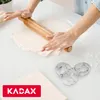 A person is rolling out dough with a rolling pin, with cookie cutters in the foreground. Podgląd zdjęcia produktu