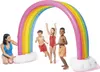 Children and an adult playing with a rainbow sprinkler in what appears to be a backyard or pool area. Produktbild-Vorschau