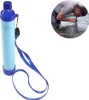 A person is drinking water from a stream using a portable water filter straw. The water filter straw is also shown separately. Produktbild-Vorschau