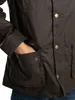 A close-up shot of a person's hand in the pocket of a brown waxed jacket. Produktbild-Vorschau