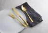 A white plate with gold cutlery and a dark gray napkin on a light gray surface. Anteprima dell’immagine prodotto