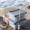 Two plastic storage boxes and a fishing rod are placed on a rocky surface near the water. Produktbild-Vorschau