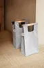 Two grey laundry bags with wooden handles are placed on a textured rug in front of a brown wall. Náhľad obrázku produktu