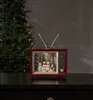 A decorative retro television with snow globes inside, placed on a dark surface in front of a Christmas tree. Podgląd zdjęcia produktu