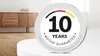 A circular badge with text and graphics is placed on a white surface in front of a wooden cabinet. Produktbild-Vorschau