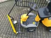 A yellow and black snow plow attachment for a riding lawn mower is shown on a paved surface. Produktbild-Vorschau