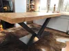 A wooden table with a metal base sits on a cowhide rug in a room with a radiator and a window. Produktbild-Vorschau