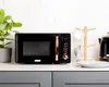 A black and copper microwave oven is displayed on a countertop with a plant and a mug tree in the background. Anteprima dell’immagine prodotto