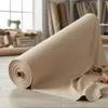 A roll of beige fabric is displayed in a sewing or crafting room setting. Podgląd zdjęcia produktu