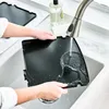 A person is rinsing a black grill plate under a faucet in a kitchen sink. Produktbild-Vorschau