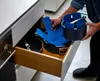 A person is putting a blue oven mitt into a kitchen drawer with pots and pans. Anteprima dell’immagine prodotto