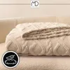 A folded beige blanket with a textured pattern is placed on a beige sofa. A logo and a circular icon with a feather and cloud are visible. Anteprima dell’immagine prodotto