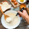 A person is using a black electric milk frother to mix ingredients in a white bowl, with eggs, flour, and lemons visible in the background. Produktbild-Vorschau