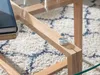 A close-up view of a wooden coffee table with a glass top, resting on a textured rug. Náhľad obrázku produktu