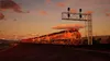 A train with multiple locomotives and cars moving along a track at sunset. Náhled obrázku produktu