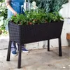 A person is watering plants in a raised garden bed. Voir les images du produit