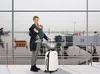 A woman with a baby in a carrier at an airport, with a suitcase. Produktbild-Vorschau