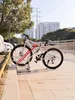 A bicycle parked in a bike rack next to a sidewalk and a body of water, with buildings and power lines in the background. Produktbild-Vorschau