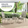 A rattan garden table and chairs set on a patio with greenery in the background. Produktbild-Vorschau