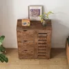 A wooden cabinet with drawers and a slatted door, decorated with a framed picture and a vase of flowers. Náhľad obrázku produktu