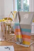 A children's blanket with a bird motif and rainbow stripes is draped over a wooden play structure in a bright, airy room. Produktbild-Vorschau