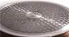 Close-up of the textured bottom of a pot or pan, showing a circular embossed logo in the center. Podgląd zdjęcia produktu