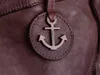A close-up of a brown leather bag with an anchor-shaped charm. Produktbild-Vorschau