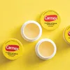 Several Carmex lip balm pots are arranged on a bright yellow background. Anteprima dell’immagine prodotto