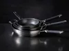 A stack of three frying pans with black handles against a dark background. Produktbild-Vorschau