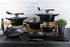 A collection of black cookware with wooden handles and lids, arranged on a dark countertop against a white brick wall. Anteprima dell’immagine prodotto