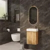 A modern bathroom with dark marble tiles, featuring a wall-mounted vanity with a wooden cabinet and a white sink, a wall-mounted toilet, a towel rack, and an oval illuminated mirror. Produktbild-Vorschau