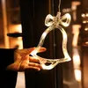 A hand holding a lit-up bell-shaped Christmas decoration with a bow, hanging in front of a window. Produktbild-Vorschau