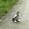 A plush toy pigeon is sitting on a paved path next to grass. Náhled obrázku produktu