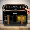 A close-up shot of a black Duronic air fryer with gold accents, placed on a wooden surface. A hand is shown pressing a button on the control panel. Produktbild-Vorschau