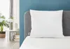 A white pillow on a bed with a blue headboard and a plant in the background. Produktbild-Vorschau
