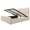A beige upholstered bed frame with its mattress support mechanism lifted, revealing storage space underneath. The bed has a tufted headboard and footboard with gold accents. Náhled obrázku produktu
